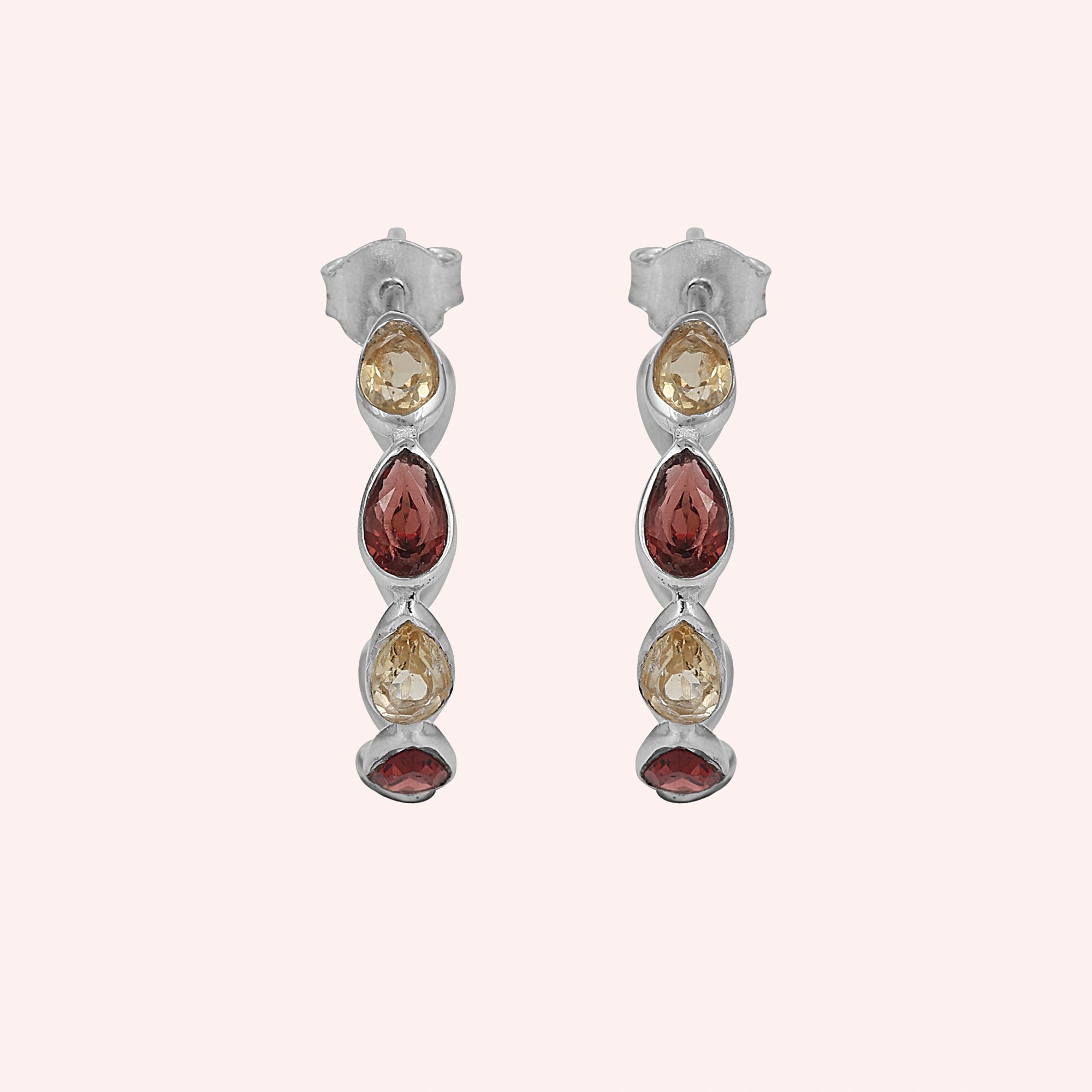 Silver hoop earrings featuring three pear cut citrine and two pear cut garnet stones on a pink background top down angle