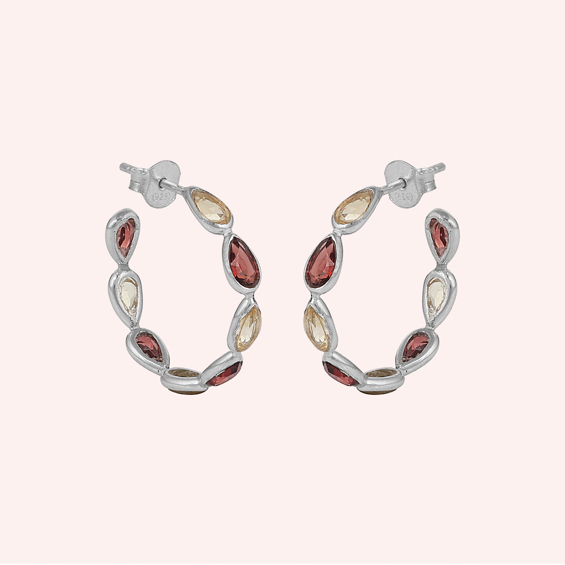Silver hoop earrings featuring alternating pear cut citrine and garnet gemstones on a pink background slightly angled view shot