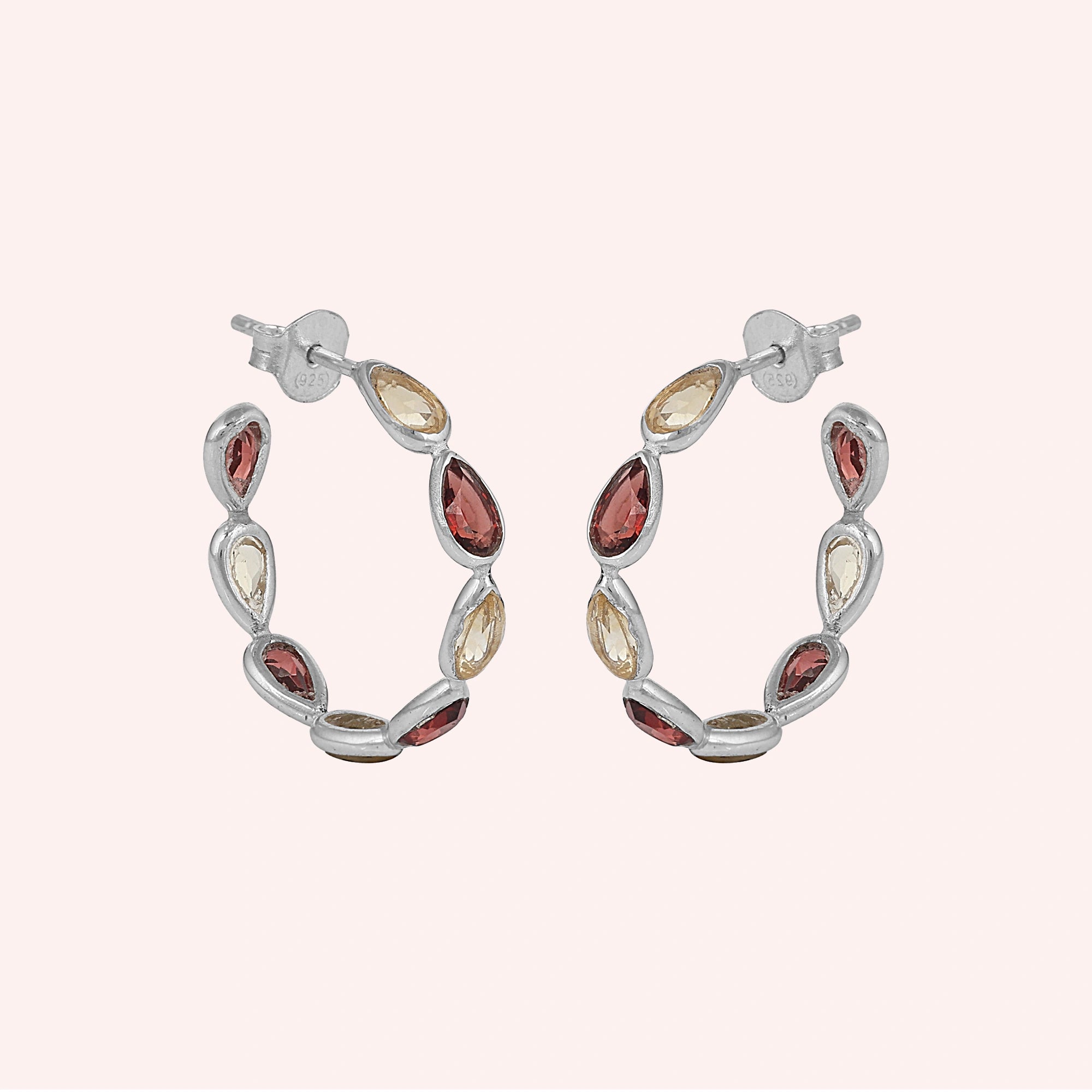 Silver hoop earrings featuring alternating pear cut citrine and garnet gemstones on a pink background slightly angled view shot