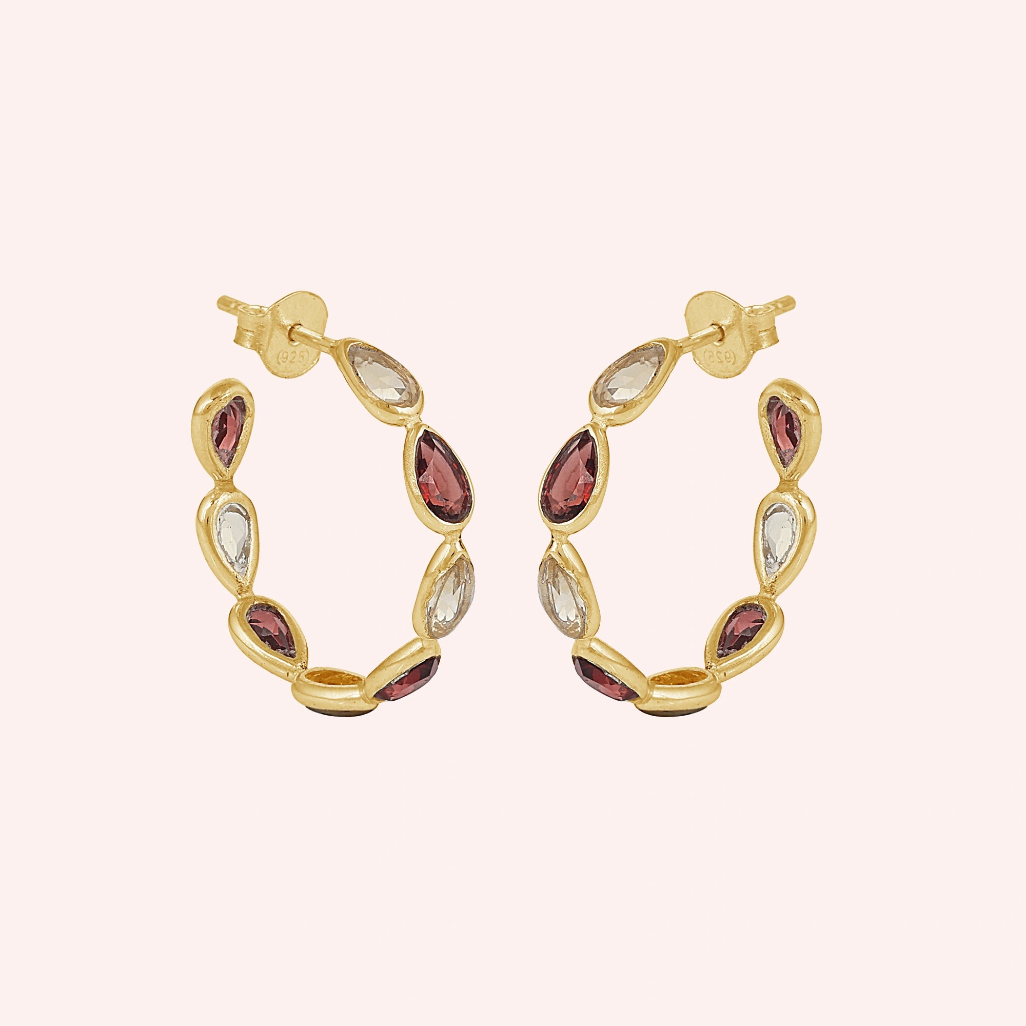 Gold plated hoop earrings featuring citrine and garnet pear cut stones on a pink background slightly angled view shot 