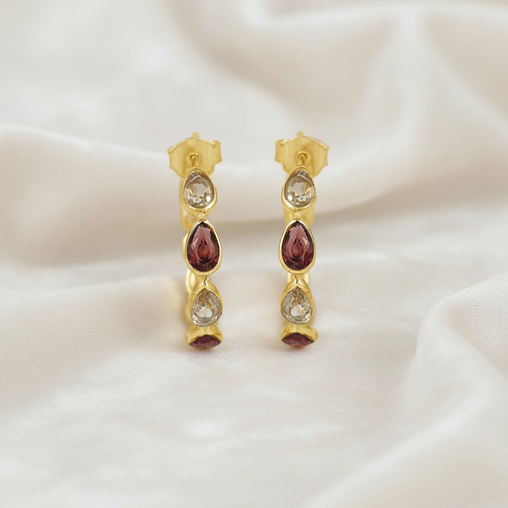 Gold plated hoop earrings with citrine and garnet pear cut stones on an off white velvet fabric close up top down angle shot