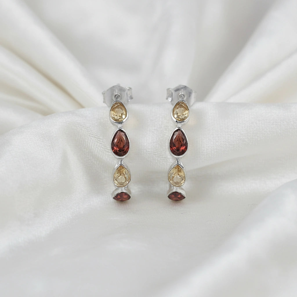 Silver hoop earrings with citrine and garnet pear cut stones on an off white velvet fabric close up top down angle shot