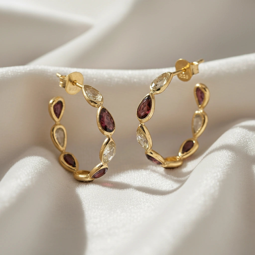 Gold plated hoop earrings featuring citrine and garnet pear cut stones on an off white velvet fabric close up angled view shot