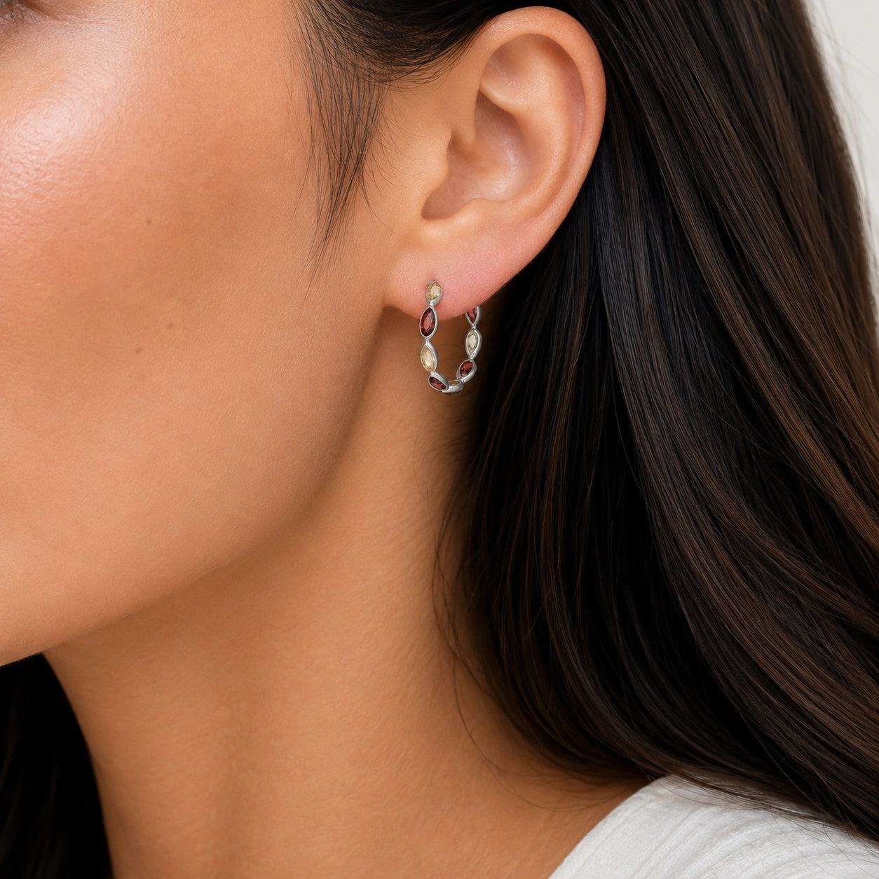 Side angle view of silver hoop earrings featuring red and yellow stones worn on the ear