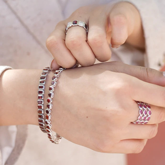 ruby band ring paired with a tennis bracelet and a heart shaped bracelet on a hand wearing a jacket against a blurred background