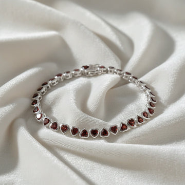 Sterling silver garnet bracelet with heart shaped red stones on a wrinkled white velvet background straight on view.