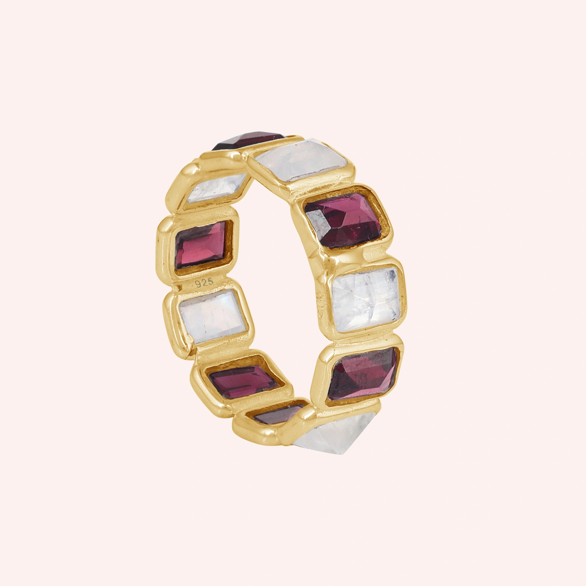 Gold-plated Garnet ring featuring alternating rectangular moonstone and rich red Garnet gemstones on a pink background slight angle.