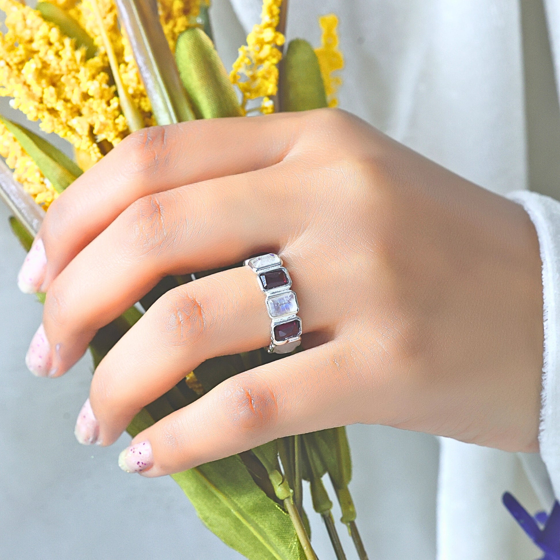 Silver Garnet ring featuring moonstone and rich Garnet gems on a hand holding yellow flowers high angle viewpoint.
