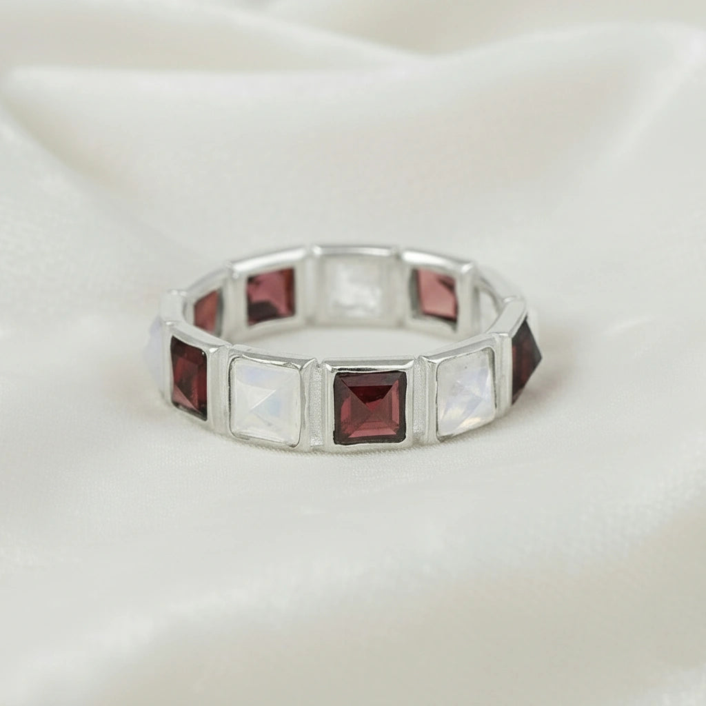Horizontal close up shot of a silver moonstone ring on a white velvet background with square moonstone and garnet stones
