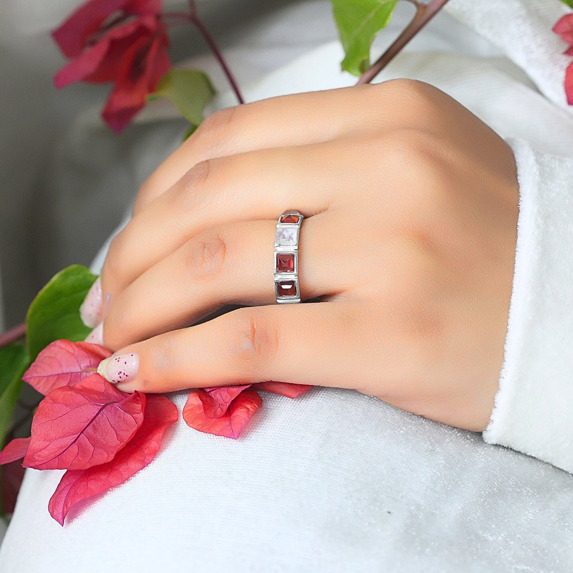 Angled close up shot of a hand wearing a silver moonstone ring on a white shirt next to a branch of red flowers
