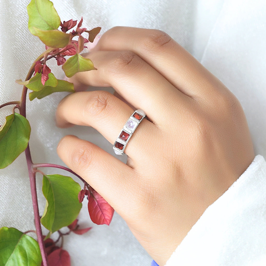 Angled close up shot of a silver moonstone ring on a white velvet background with square moonstone and garnet stones