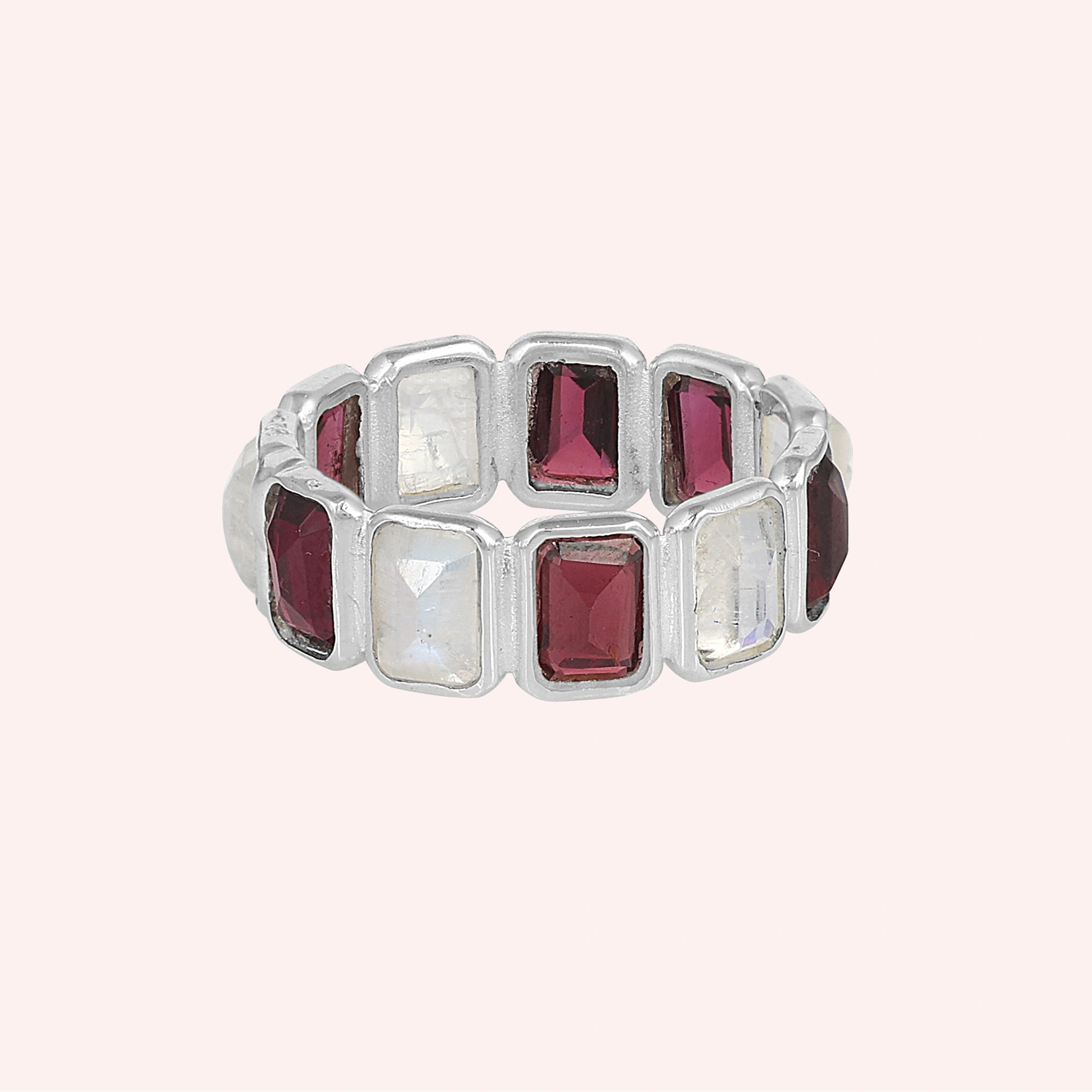 Silver Garnet ring featuring alternating rectangular gemstones and moonstones on a plain pink background front view.