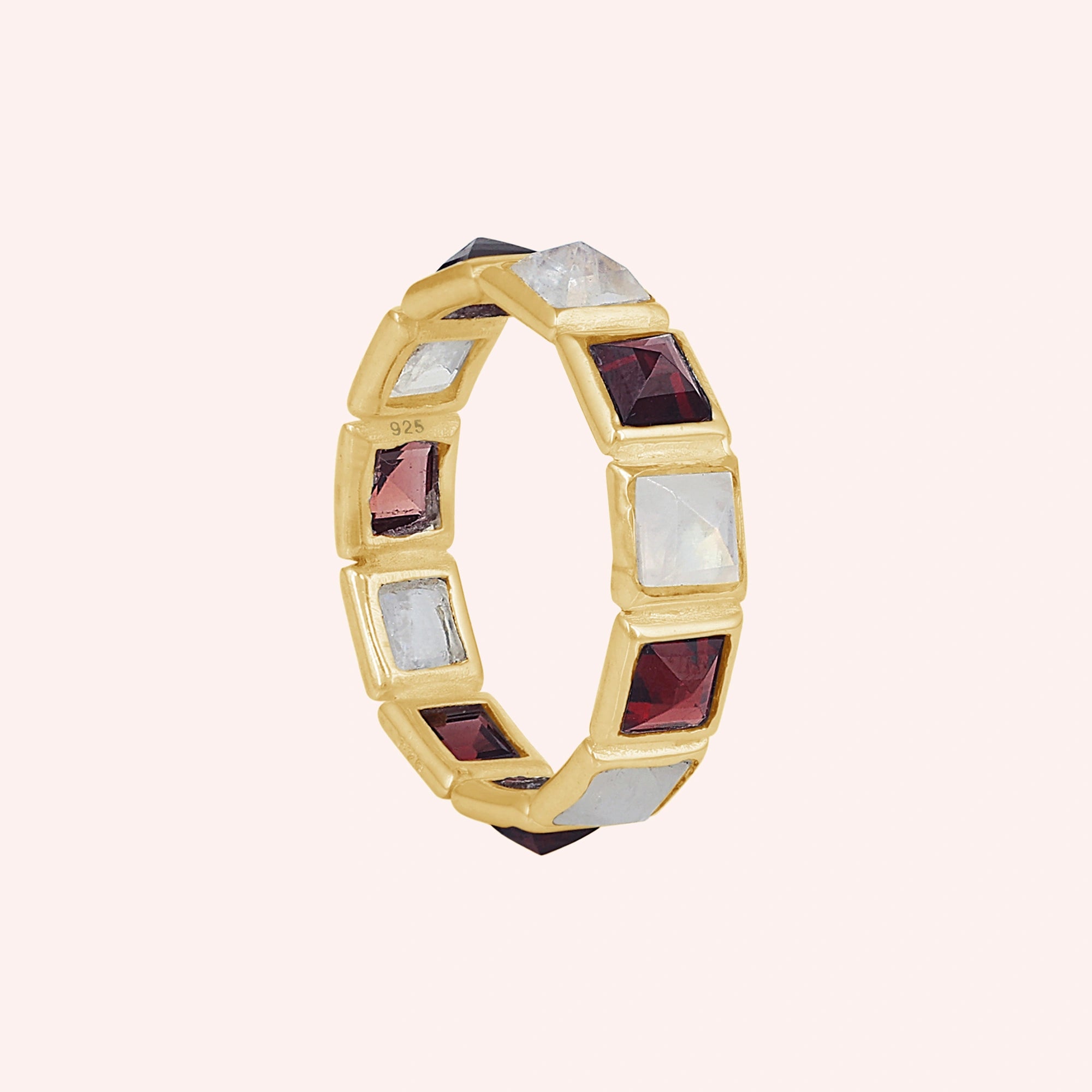 Angled shot of a gold-plated silver moonstone ring on a light pink background with alternating square moonstone and garnet