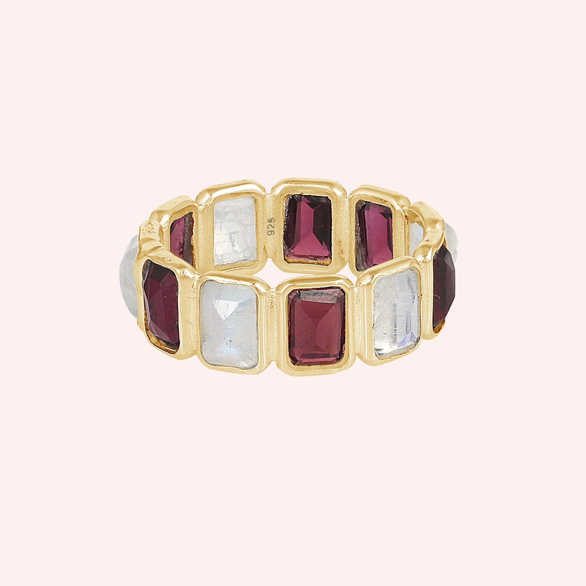Gold-plated Garnet ring featuring alternating rectangular moonstone and rich red Garnet gemstones on a pink background front view.