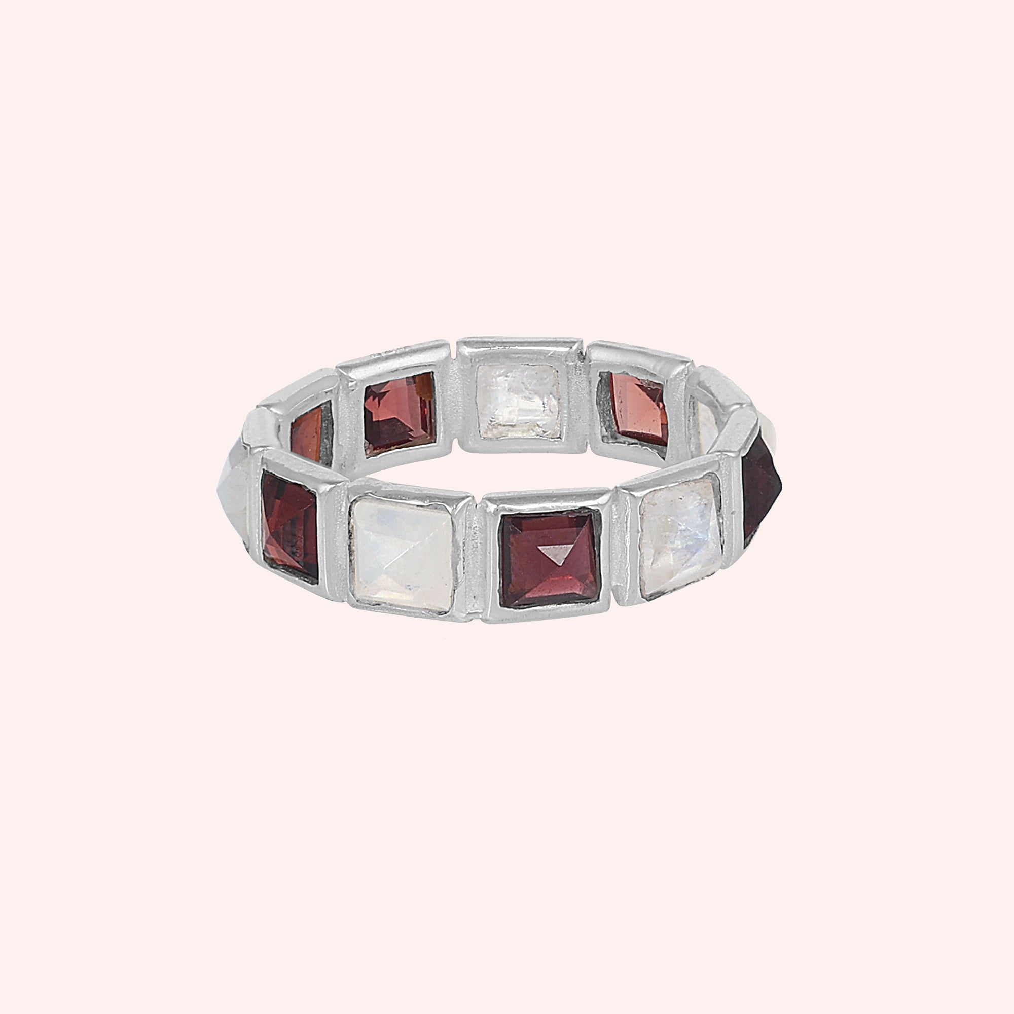 Horizontal shot of a silver moonstone ring on a light pink background with alternating square moonstone and garnet stones