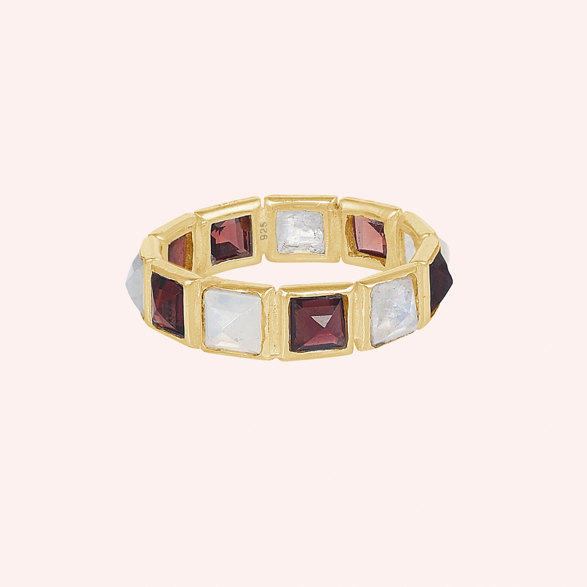 Horizontal shot of a gold-plated silver moonstone ring on a light pink background with alternating square moonstone and garnet