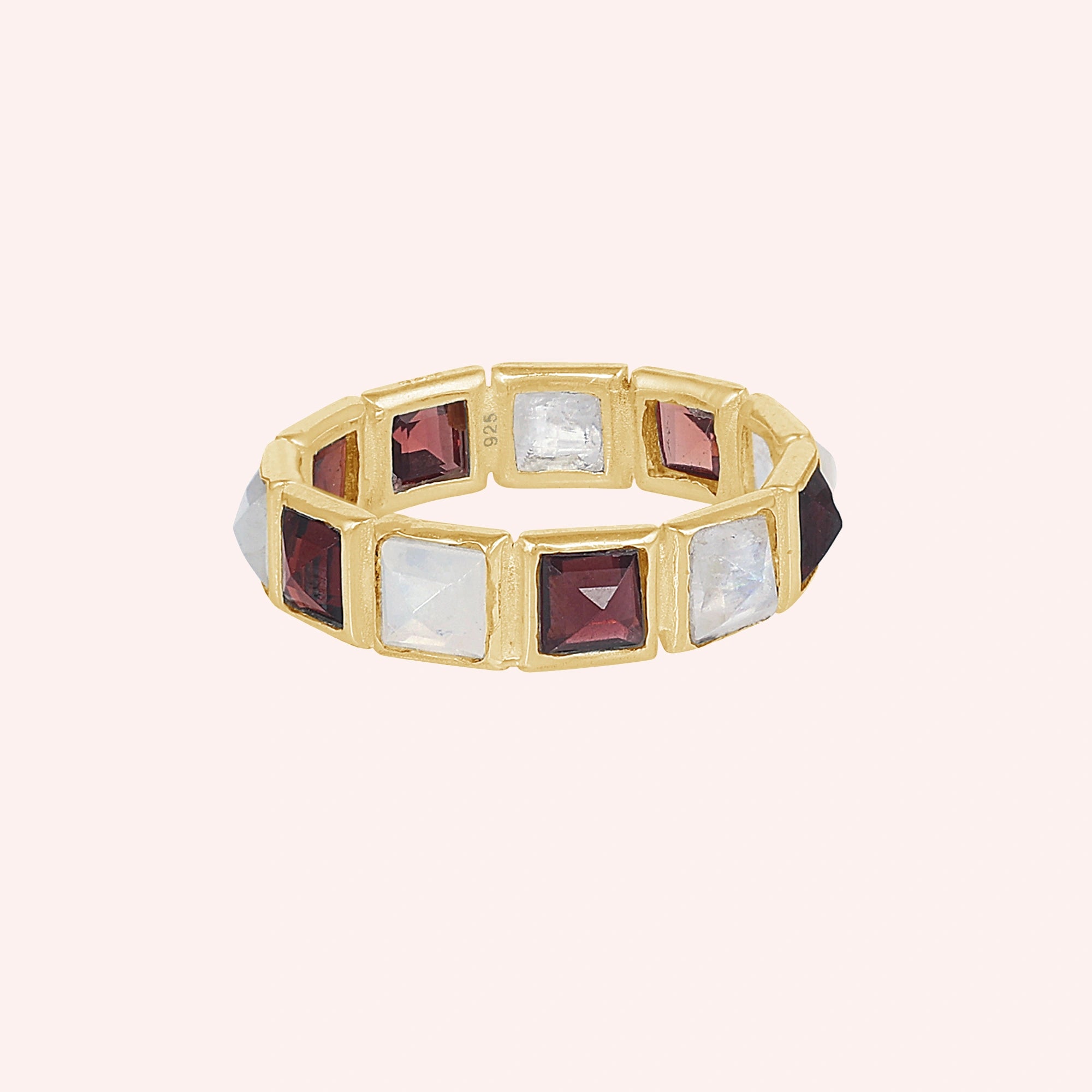Horizontal shot of a gold-plated silver moonstone ring on a light pink background with alternating square moonstone and garnet