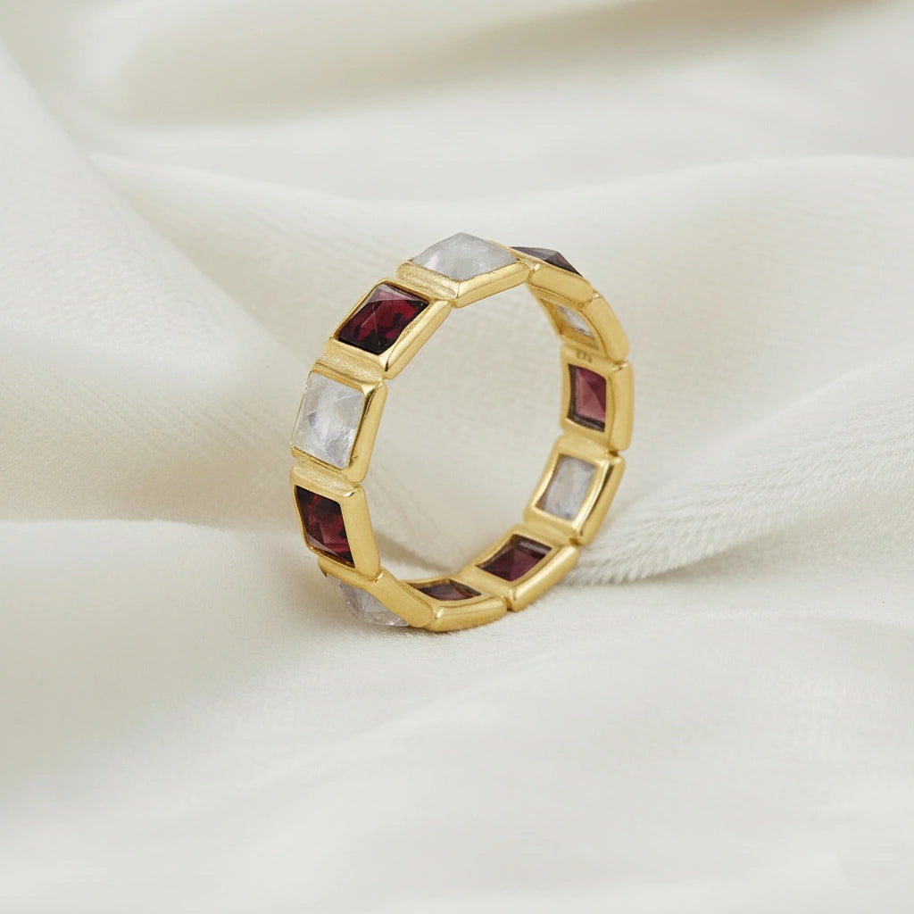 Angled close up shot of a gold-plated silver moonstone ring on a white velvet background with square moonstone and garnet