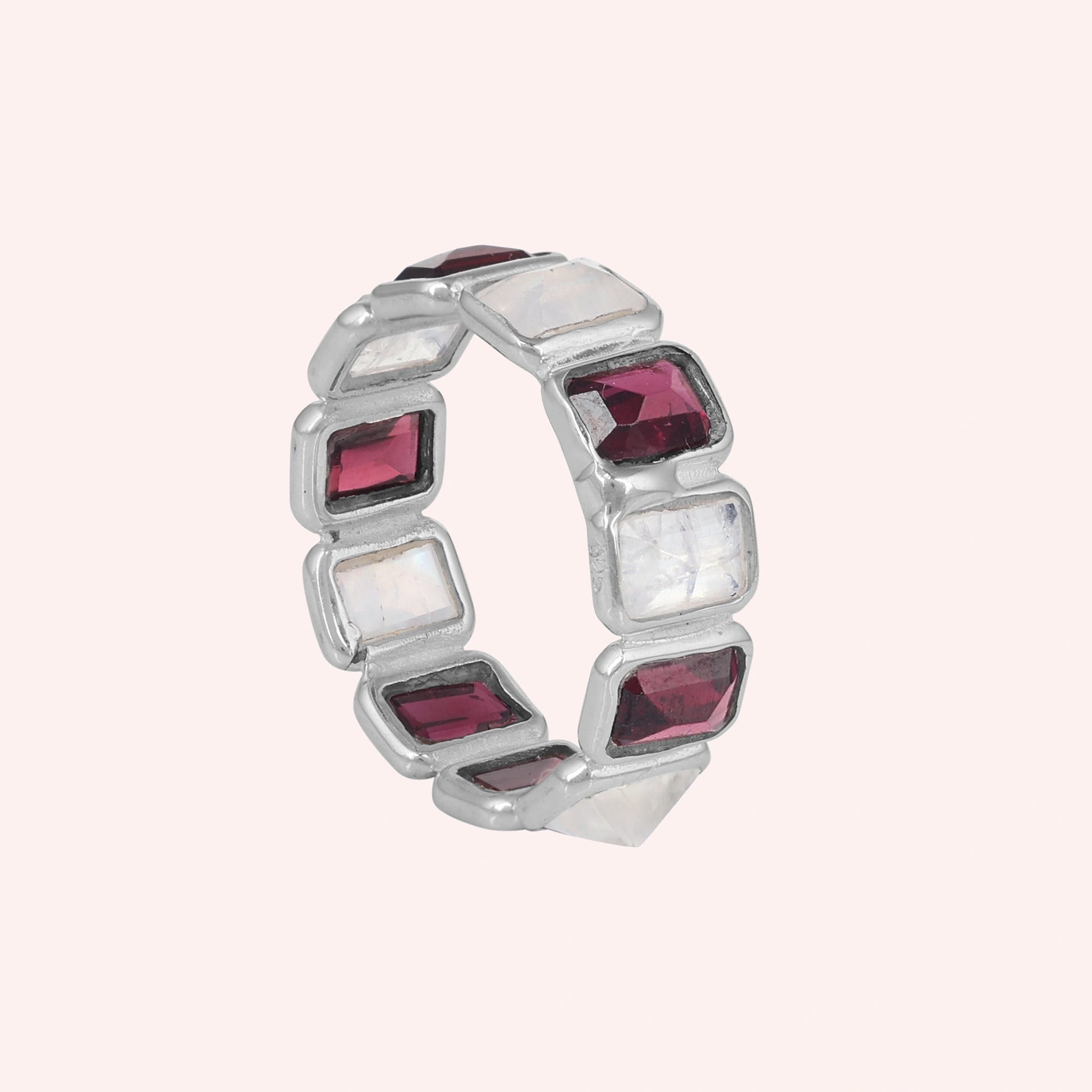 Silver Garnet ring featuring alternating rectangular moonstone and rich red Garnet gemstones on a pink background tilted angle.