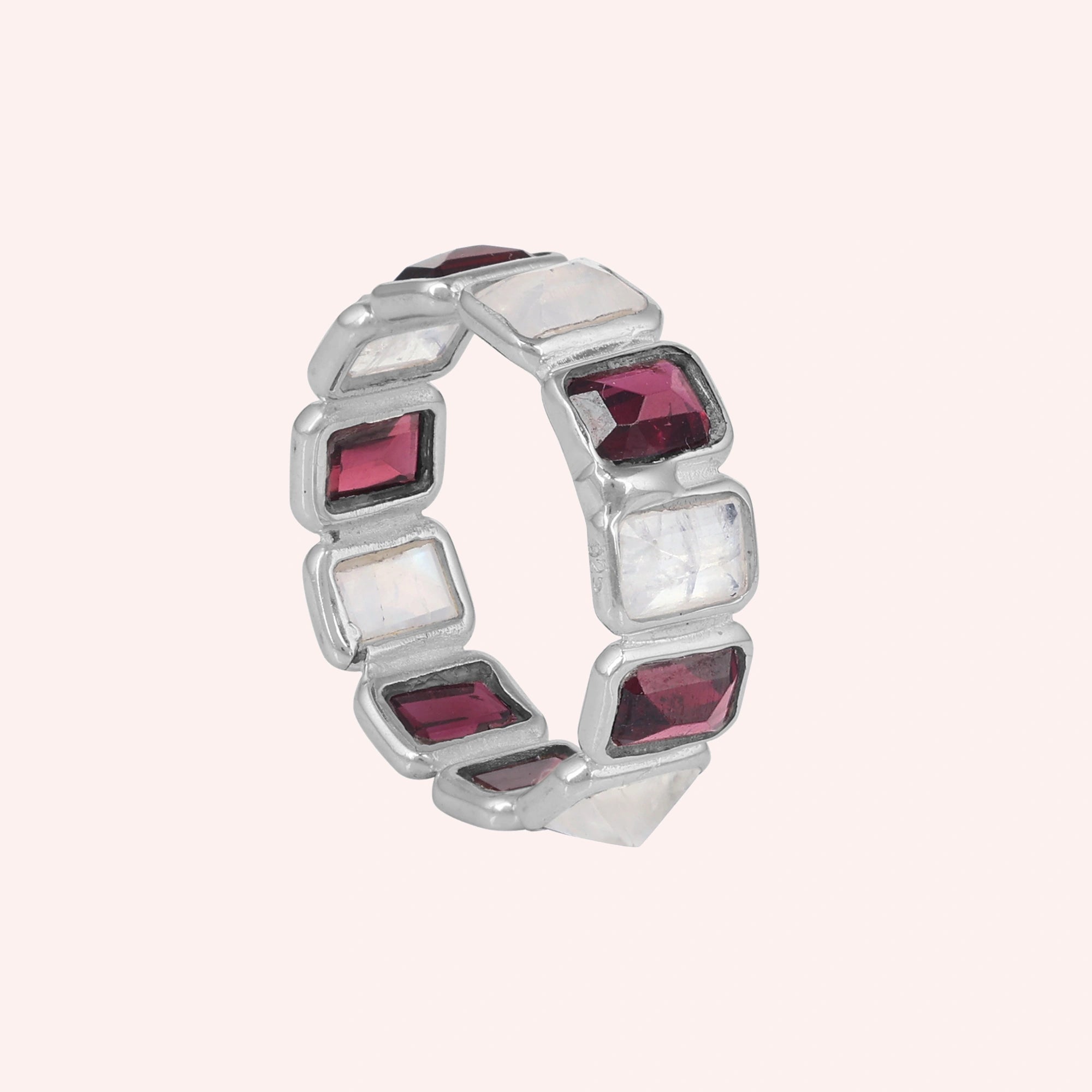 Silver Garnet ring featuring alternating rectangular moonstone and rich red Garnet gemstones on a pink background tilted angle.
