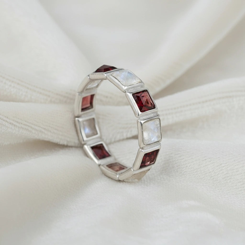 Angled close up shot of a silver moonstone ring on a white velvet background with square moonstone and garnet stones