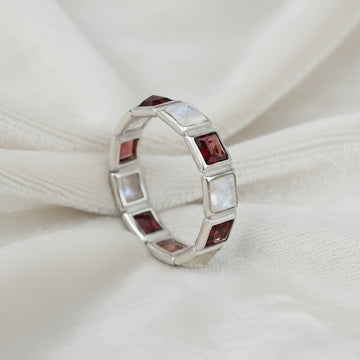 Angled close up shot of a silver moonstone ring on a white velvet background with square moonstone and garnet stones