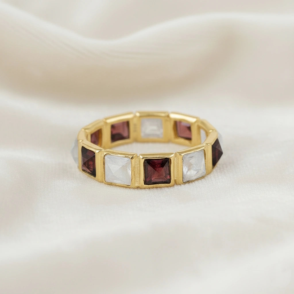 Horizontal close up shot of a gold-plated silver moonstone ring on a white velvet background with square moonstone and garnet