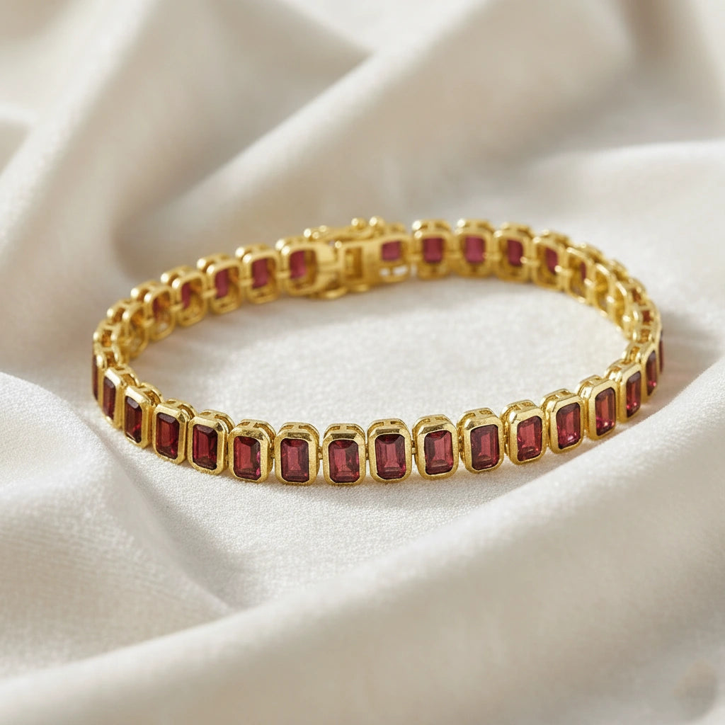 Gold plated tennis bracelet with rectangular red garnet gemstones on a wrinkled off white velvet fabric shot top down angle