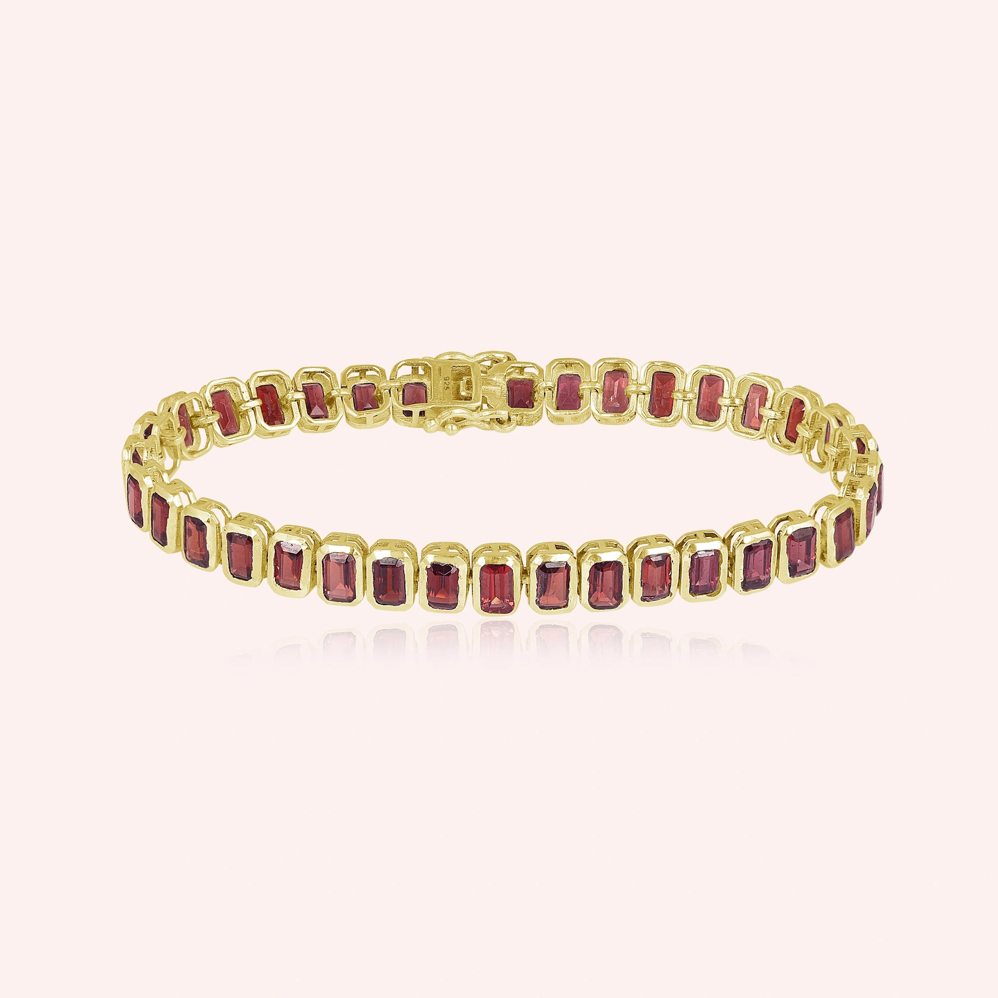 Gold plated tennis bracelet with rectangular red garnet gemstones on a blush pink background studio shot top down angle