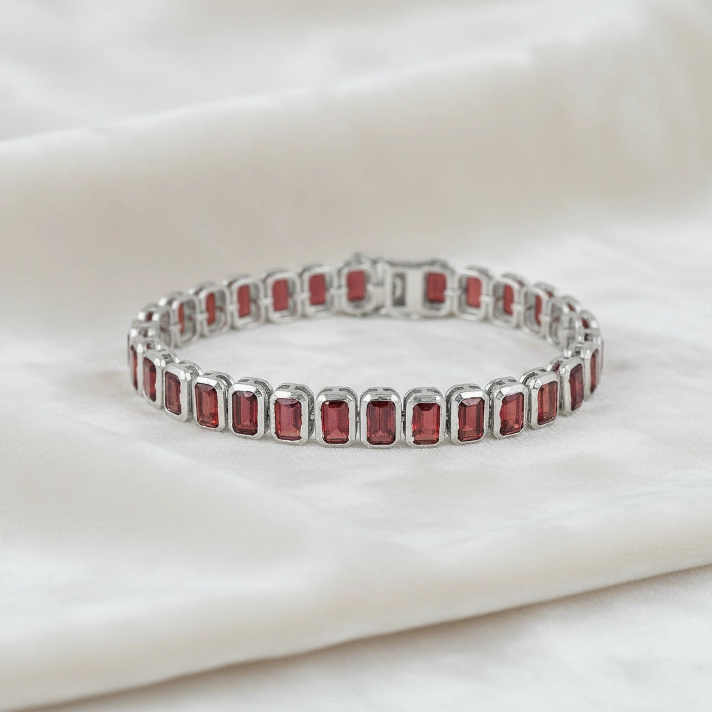 sterling silver tennis bracelet with rectangular red garnet gemstones on a wrinkled off white velvet fabric top down angle shot