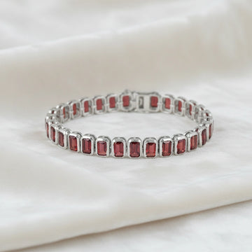 sterling silver tennis bracelet with rectangular red garnet gemstones on a wrinkled off white velvet fabric top down angle shot