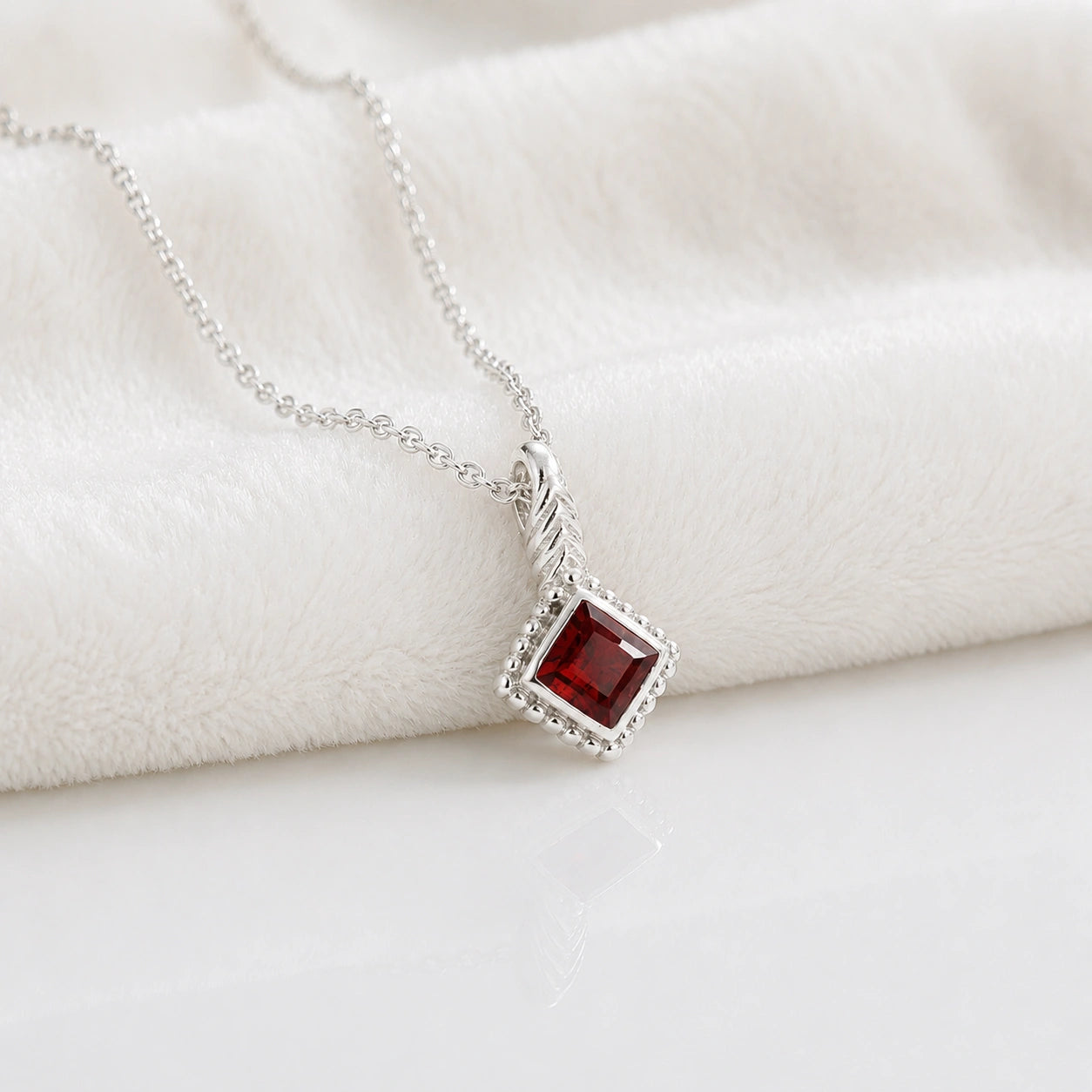 Birthstone_necklace_in_sterling_silver_with_square_cut_garnet_pendant_in_slightly_angled_view_on_soft_white_fabric_background