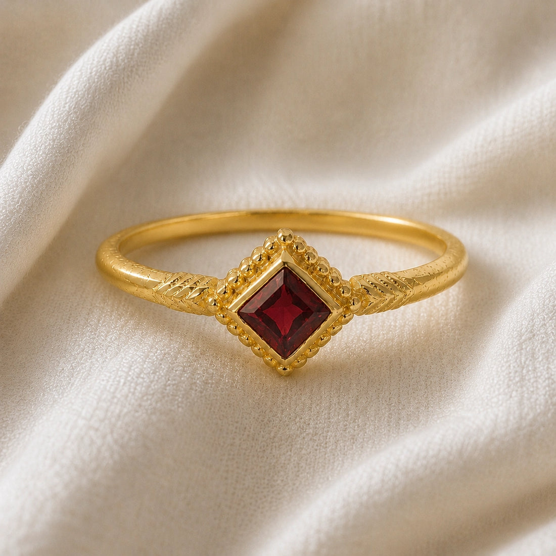 Princess_cut_ring_gold_plated_silver_with_square_garnet_and_detailed_band_front_angle_view_on_soft_fabric_background