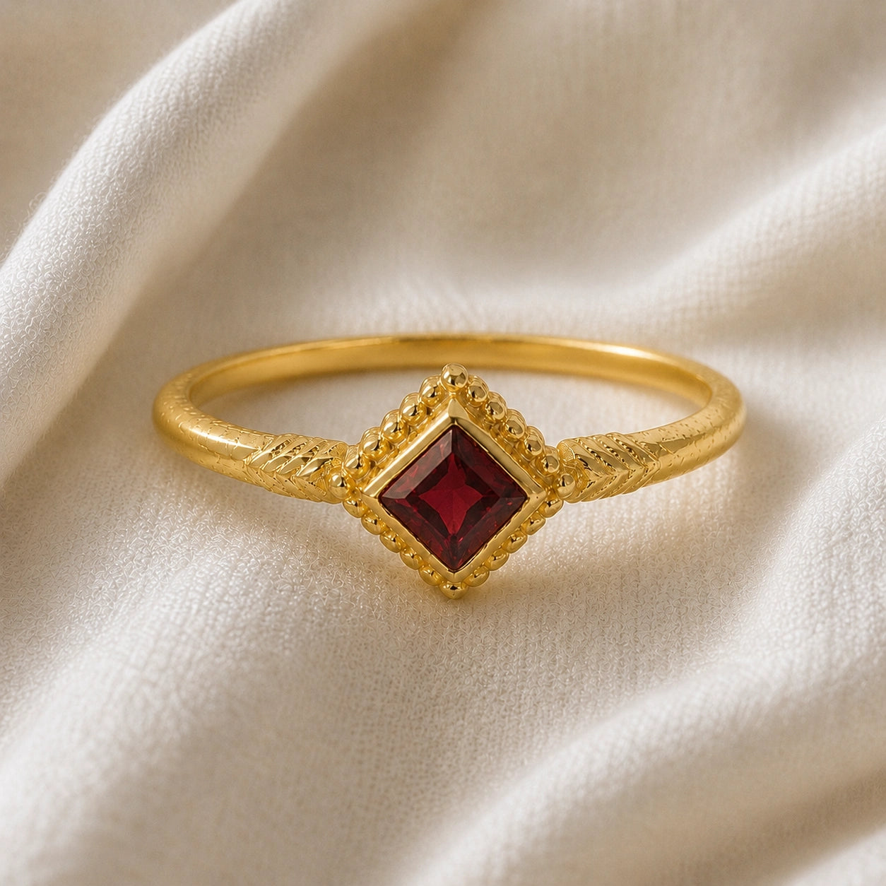 Princess_cut_ring_gold_plated_silver_with_square_garnet_and_detailed_band_front_angle_view_on_soft_fabric_background