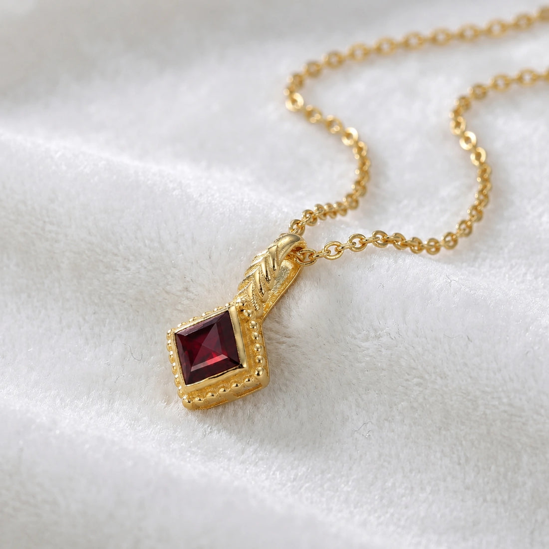 Birthstone_necklace_in_gold_plated_silver_with_square_cut_garnet_pendant_in_slightly_angled_view_on_soft_white_fabric_background