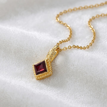 Birthstone_necklace_in_gold_plated_silver_with_square_cut_garnet_pendant_in_slightly_angled_view_on_soft_white_fabric_background