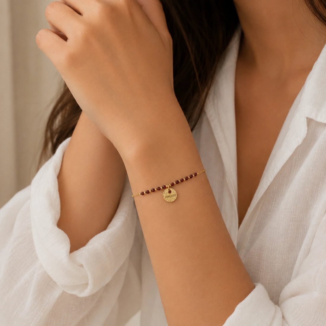 Birthstone_bracelet_in_gold_plated_silver_with_January_charm_and_garnet_beads_on_fine_chain_on_solid_pink_background