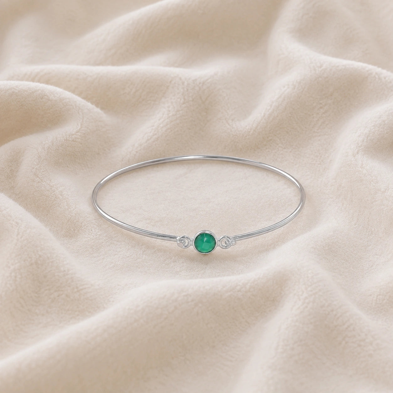 Gemstone_bracelet_in_sterling_silver_with_a_round_green_onyx_stone_at_front_angle_view_on_soft_fabric_background