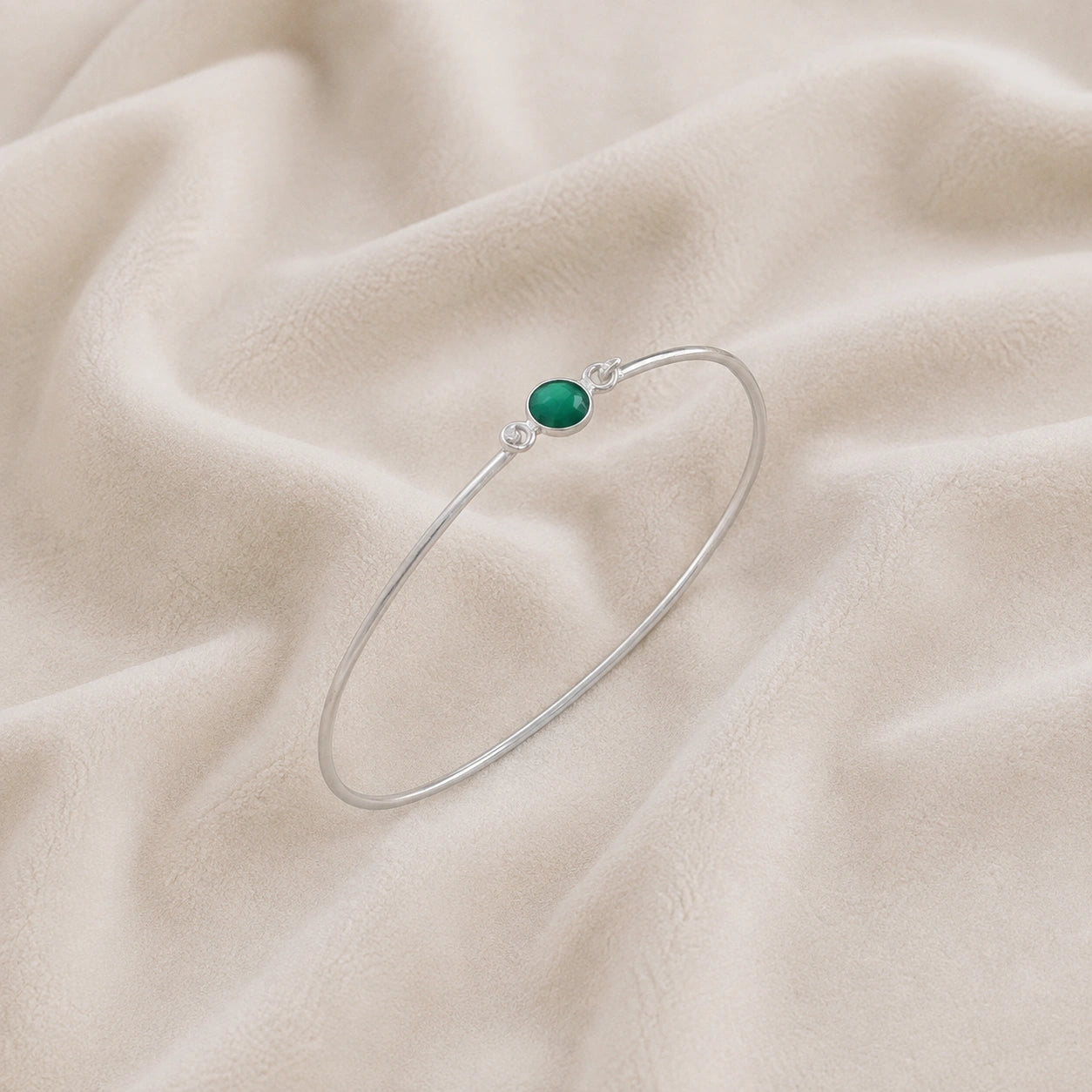 Gemstone_bracelet_in_sterling_silver_with_a_round_green_onyx_stone_at_slight_angle_view_on_soft_fabric_background