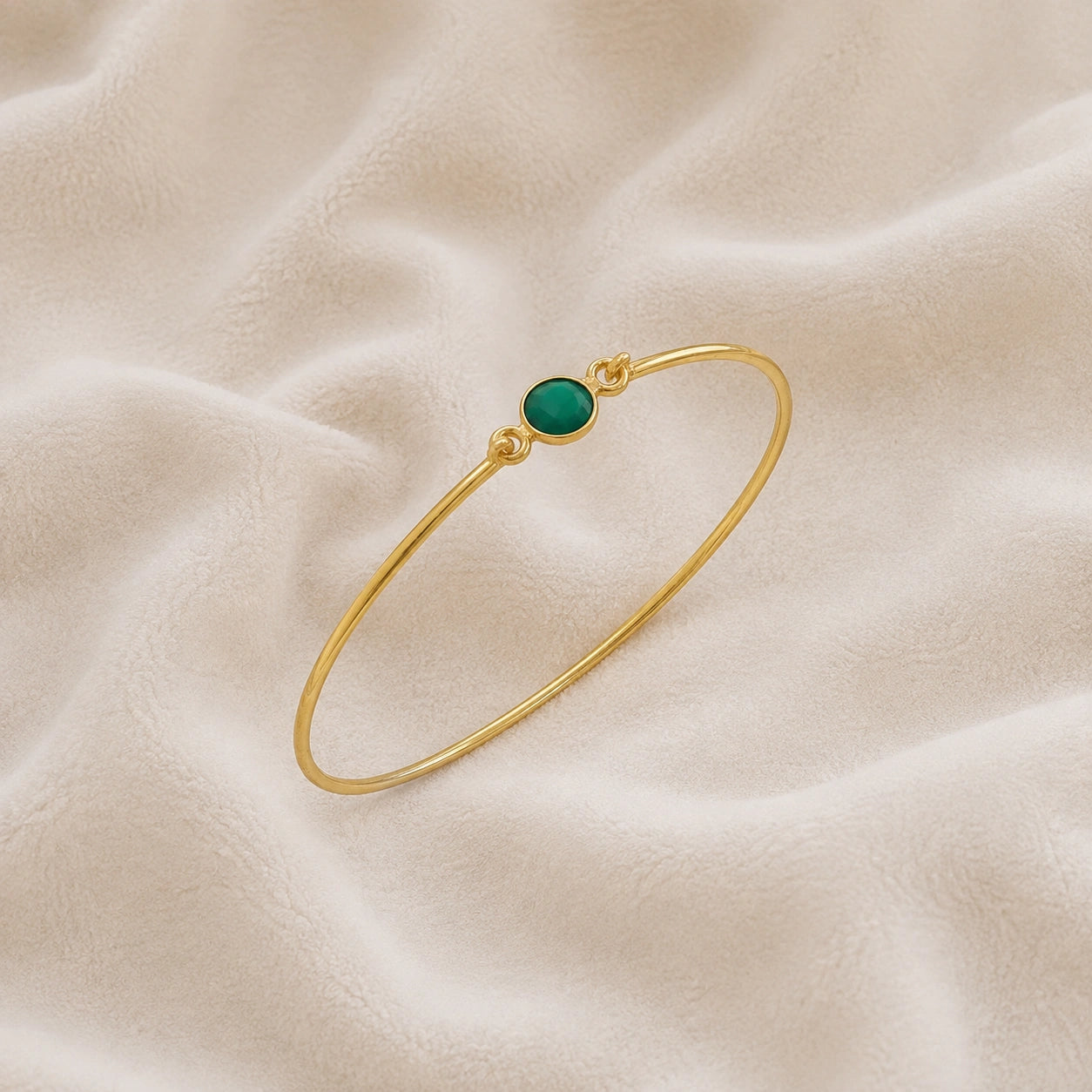 Gemstone_bracelet_in_gold_plated_silver_with_a_round_green_onyx_stone_at_slight_angle_view_on_soft_fabric_background