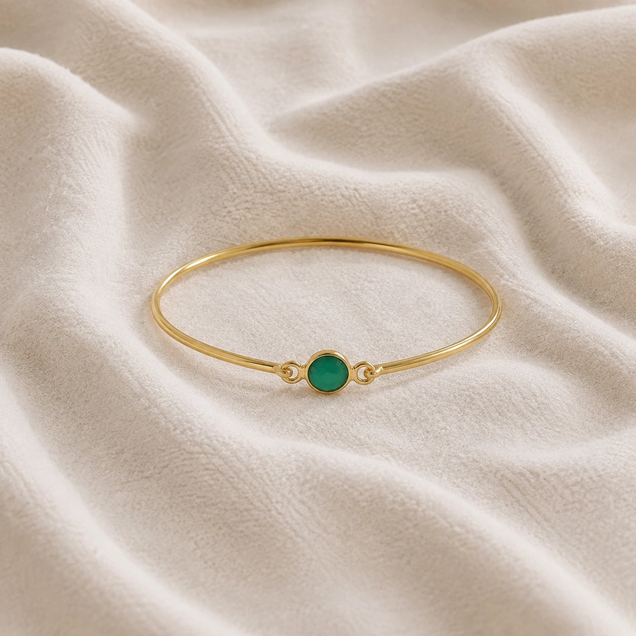 Gemstone_bracelet_in_gold_plated_silver_with_a_round_green_onyx_stone_at_front_angle_view_on_soft_fabric_background