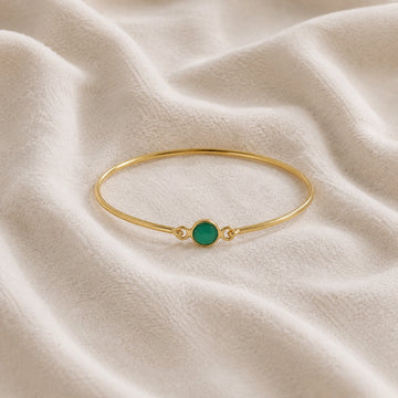 Gemstone_bracelet_in_gold_plated_silver_with_a_round_green_onyx_stone_at_front_angle_view_on_soft_fabric_background
