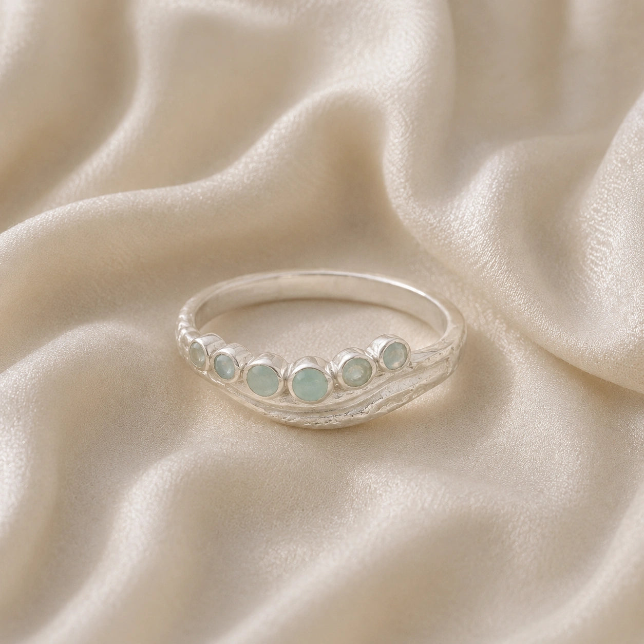 Gemstone_ring_in_sterling_silver_at_front_angle_featuring_amazonite_stones_in_a_curve_design_on_soft_fabric_background