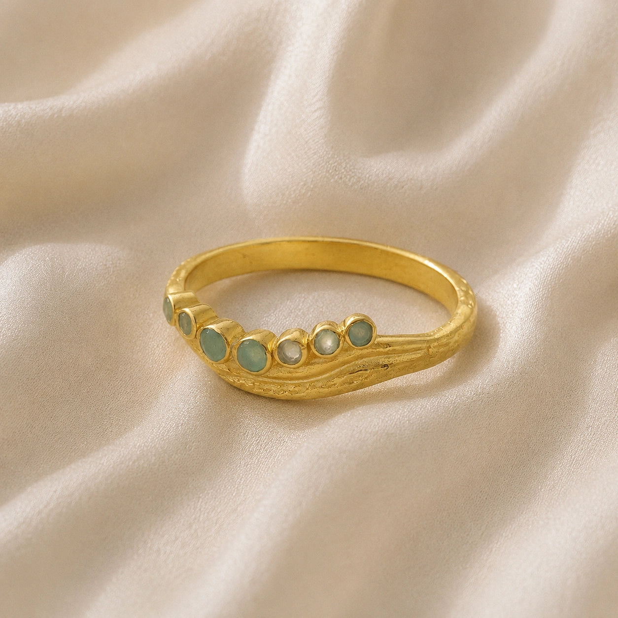 Gemstone_ring_in_gold_plated_silver_at_slightly_angled_featuring_amazonite_stones_in_a_curve_design_on_soft_fabric_background