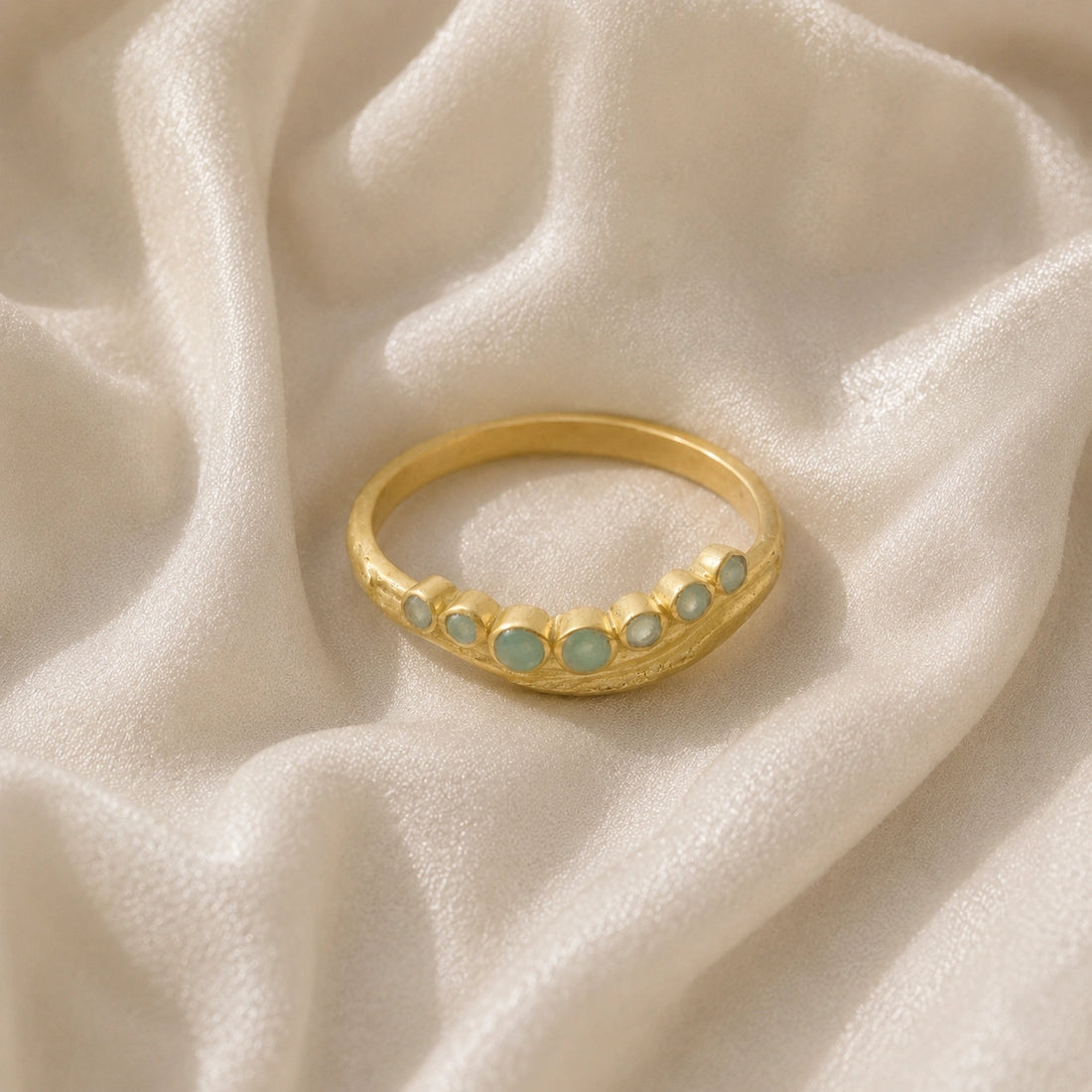 Gemstone_ring_in_gold_plated_silver_at_front_angle_featuring_amazonite_stones_in_a_curve_design_on_soft_fabric_background