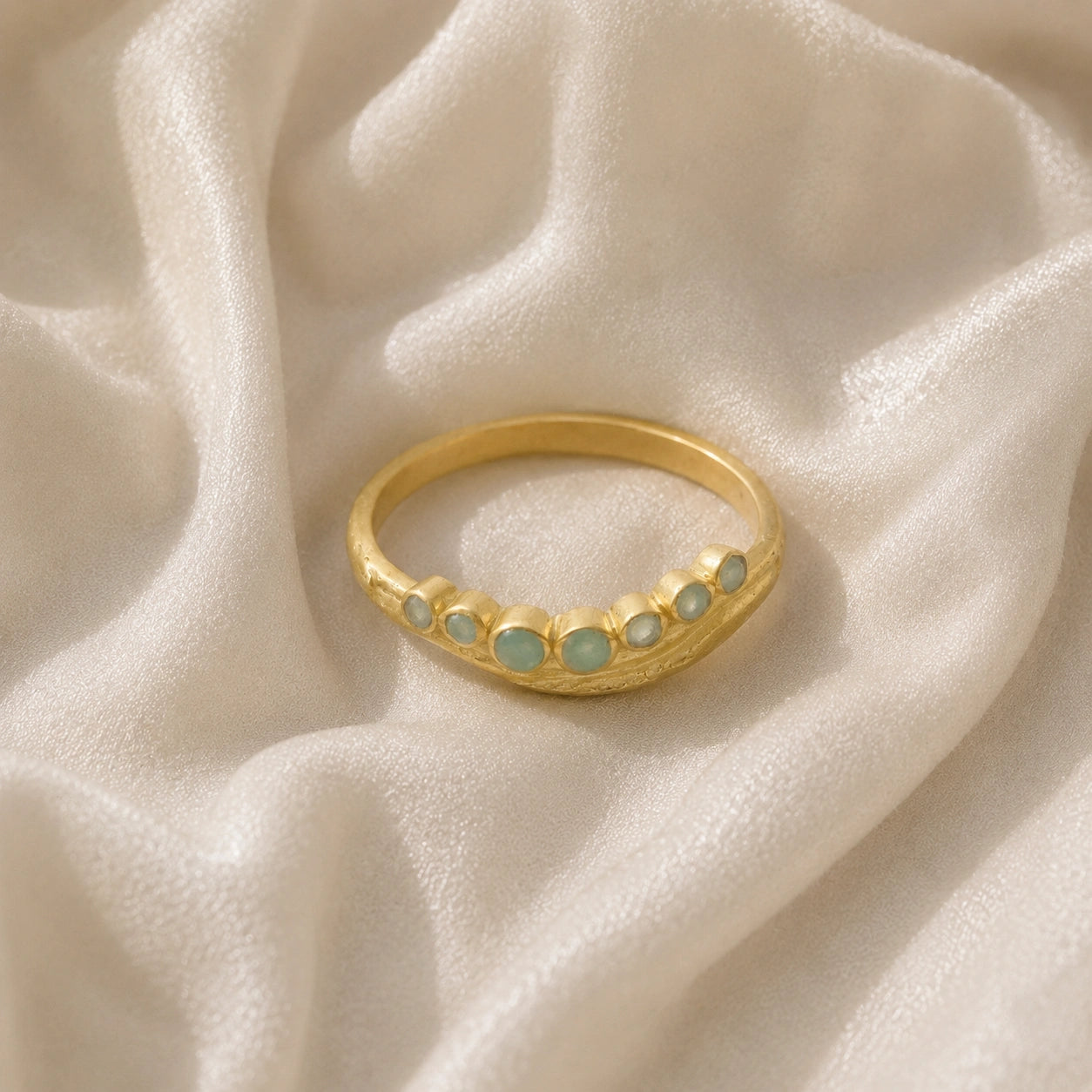 Gemstone_ring_in_gold_plated_silver_at_front_angle_featuring_amazonite_stones_in_a_curve_design_on_soft_fabric_background
