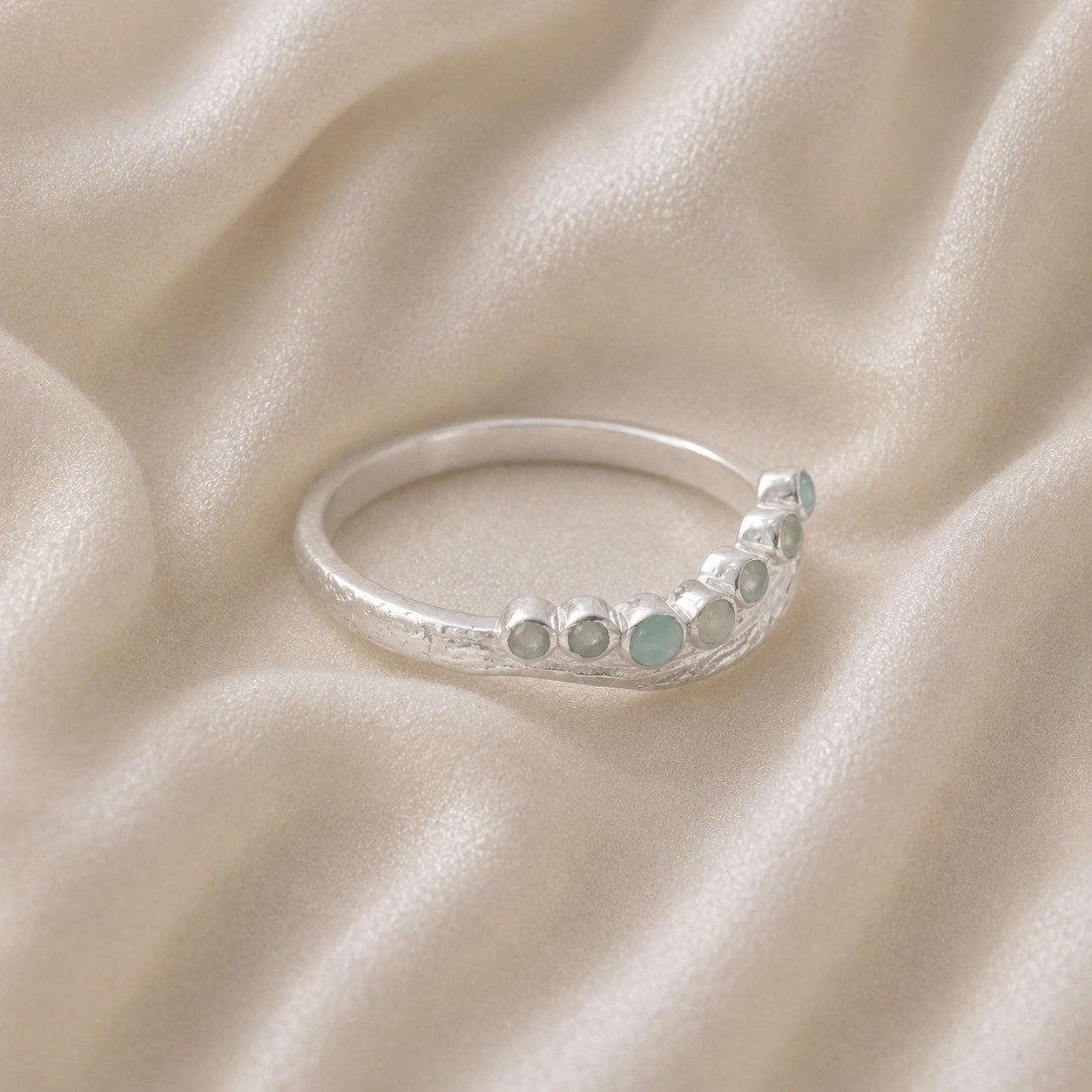 Gemstone_ring_in_sterling_silver_at_slightly_angled_featuring_amazonite_stones_in_a_curve_design_on_soft_fabric_background