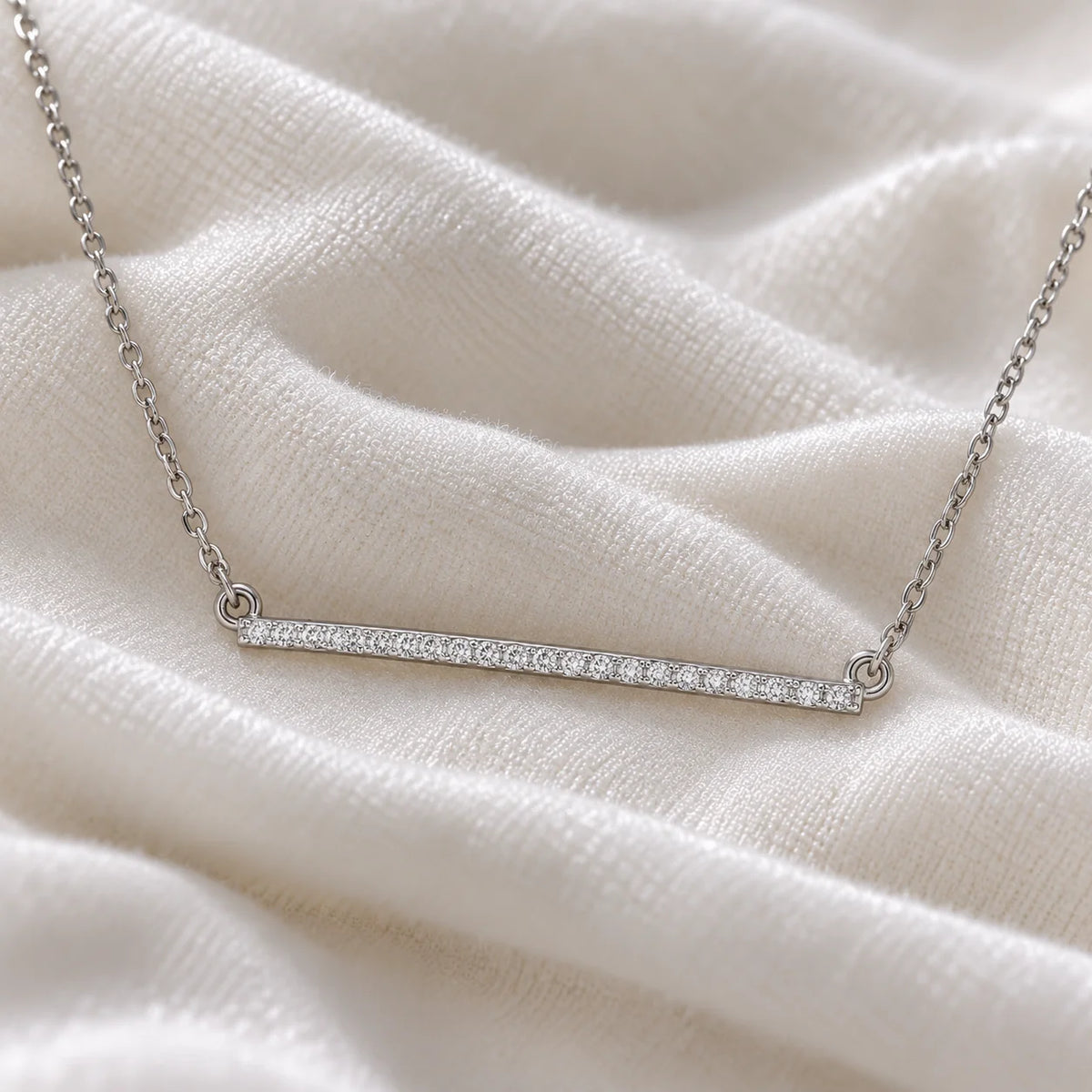 Gemstone_necklace_in_sterling_silver_in_a_bar_design_with_CZ_stones_at_front_angle_view_on_soft_fabric_background