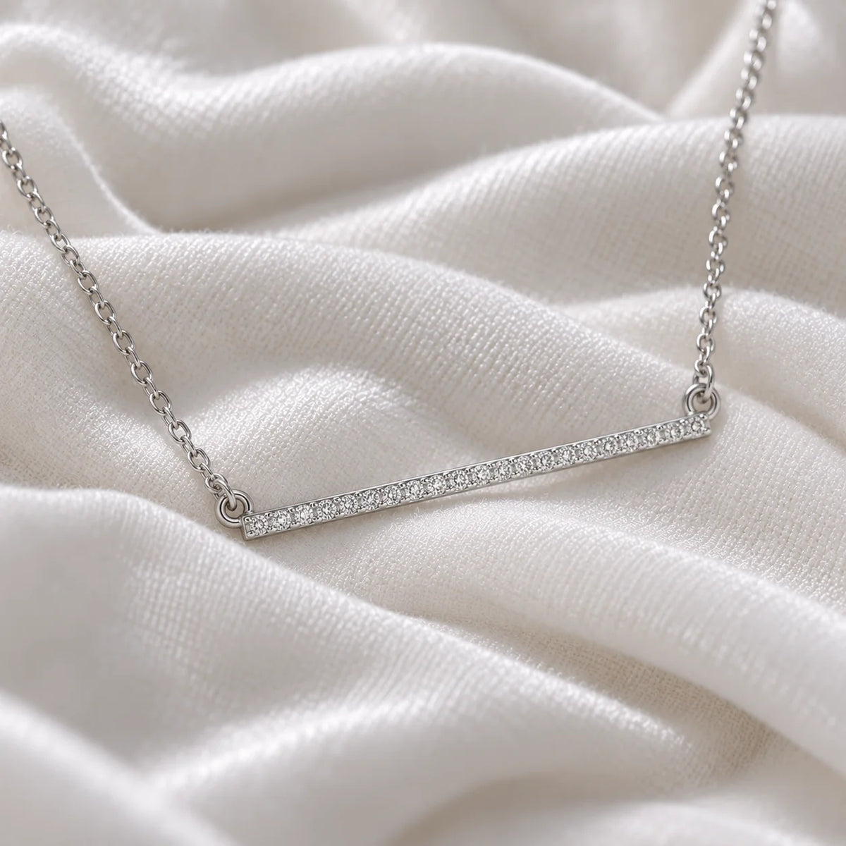 Gemstone_necklace_in_sterling_silver_in_a_bar_design_with_CZ_stones_at_side_angle_view_on_soft_fabric_background