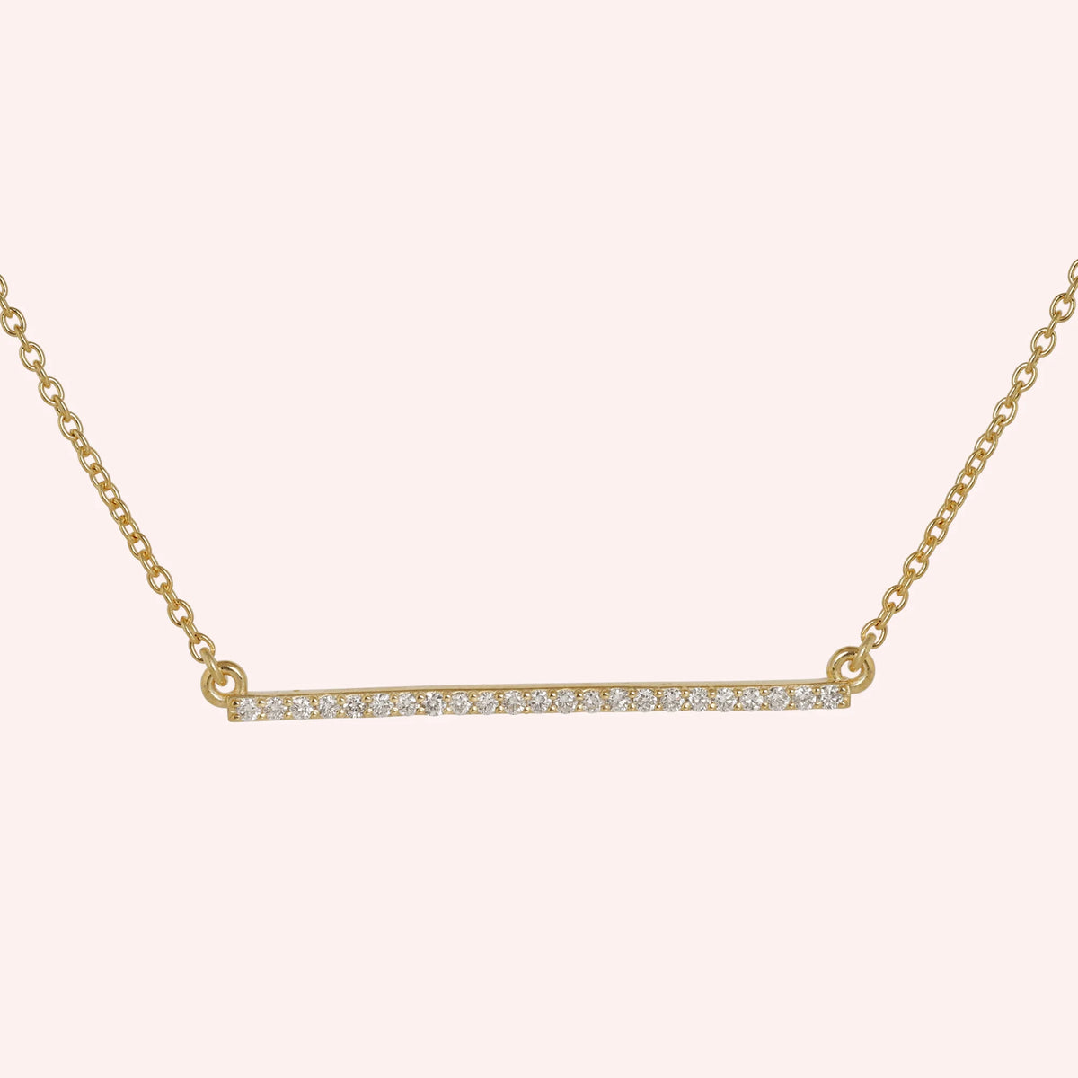 Gemstone_necklace_in_gold_plated_silver_in_a_bar_design_with_CZ_stones_at_front_angle_view_on_solid_pink_background
